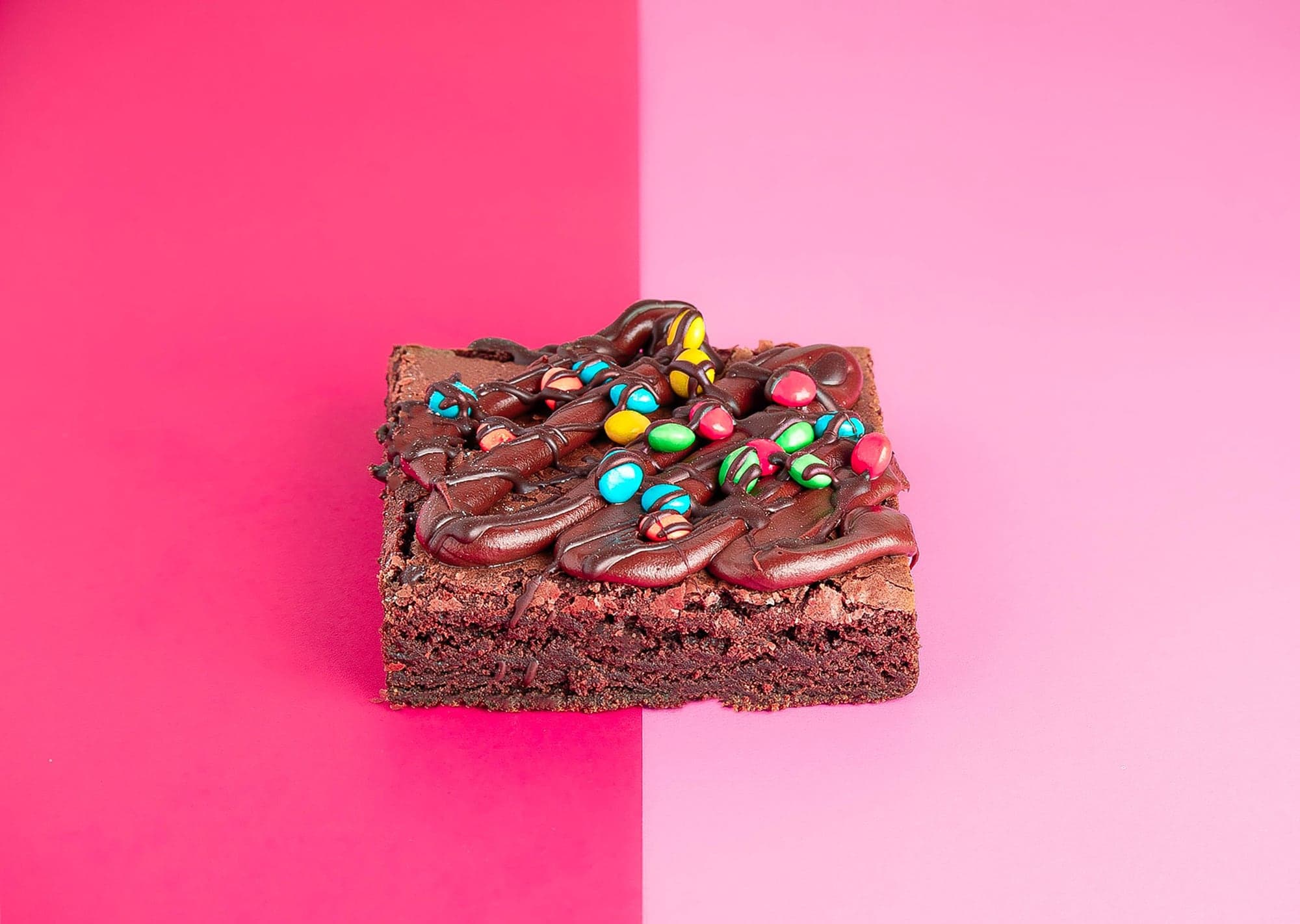 Brownie con frosting y confites de colores sobre fondo rosado