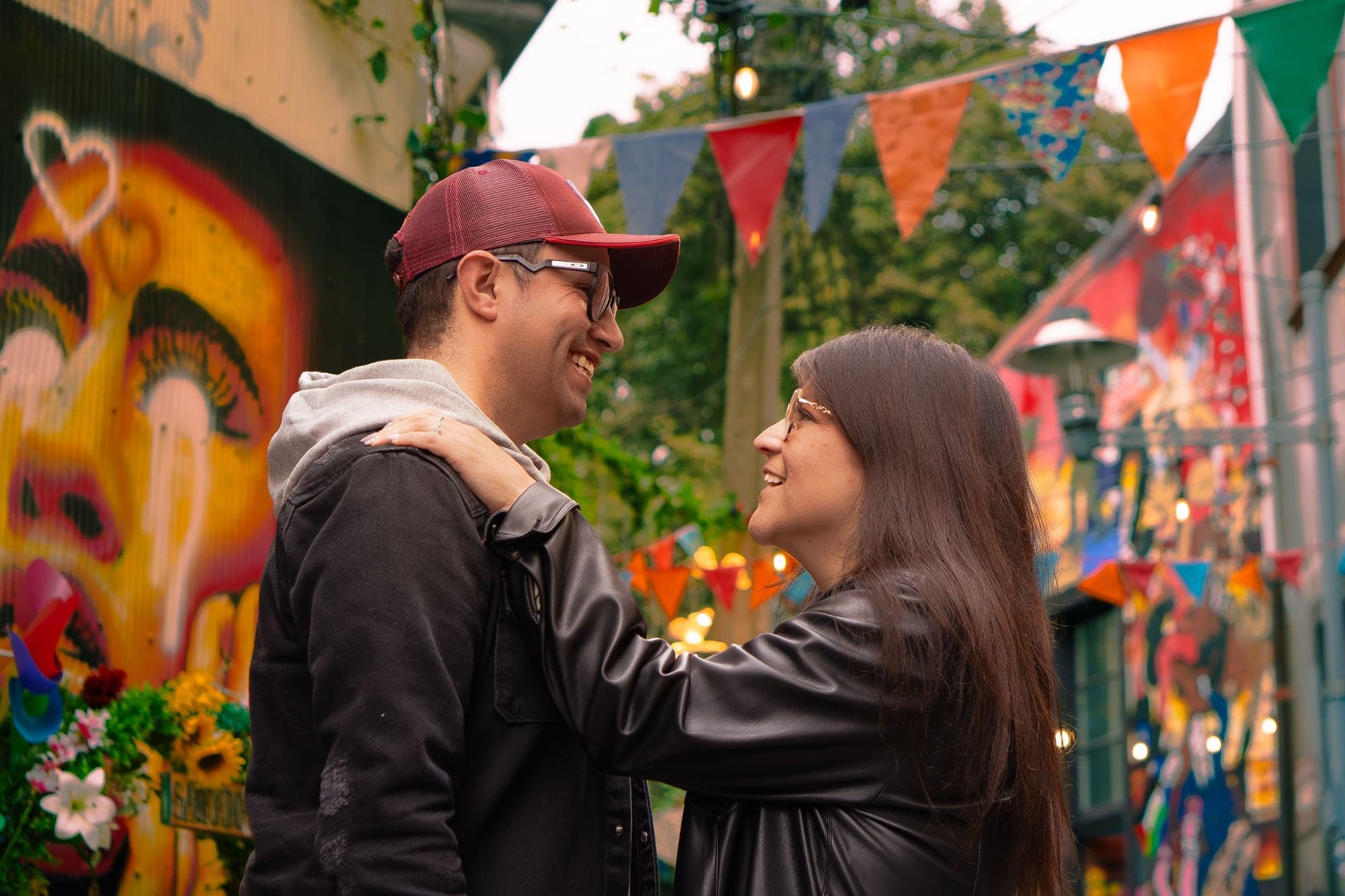 Valeska y Luis se miran sonriendo frente a un mural colorido