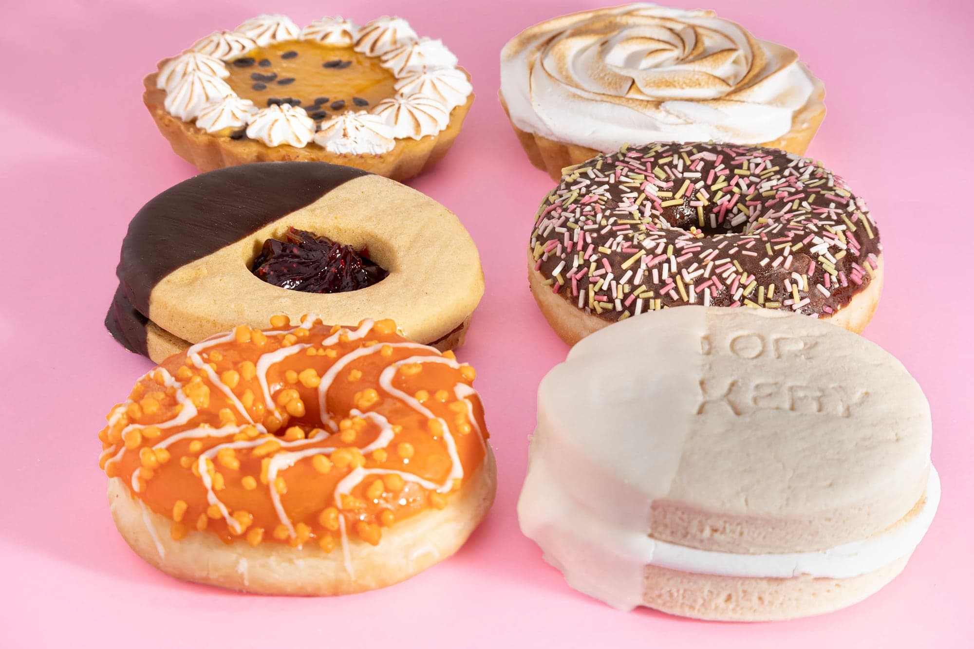 Selección de productos Fior Bakery sobre fondo rosado: tartaletas, alfajores y donas